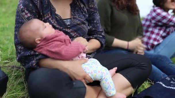 Madre sosteniendo a su bebé en sus brazos mientras está sentado en la hierba — Vídeo de stock