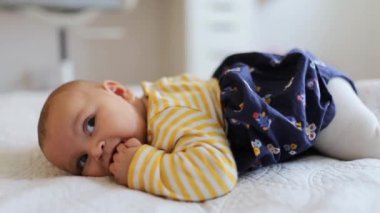 Baby Girl Lying Down on a White Bed With Her Fingers on Her Mouth