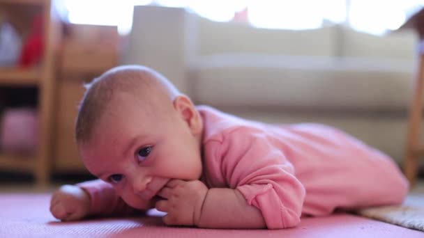 Bebê menina deitada em um tapete rosa com os dedos na boca — Vídeo de Stock