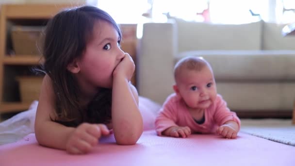 Little Girl Laughing and Lying Down Next to her Baby Sister on a Pink Rug — Vídeo de Stock