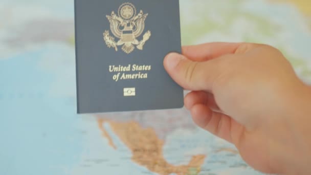 Рука держит паспорт Соединенных Штатов Америки с картой Северной Америки за спиной — стоковое видео