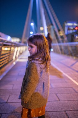 Little girl looking over her shoulder on a cable-stayed bridge during nighttime