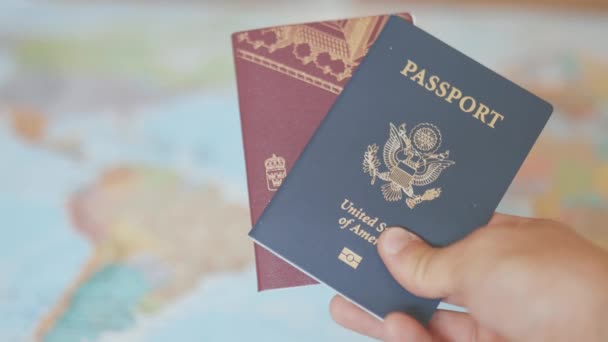 एक रंगीत जागतिक नकाशा समोर एक अमेरिकन आणि स्वीडिश पासपोर्ट हाताळणे — स्टॉक व्हिडिओ
