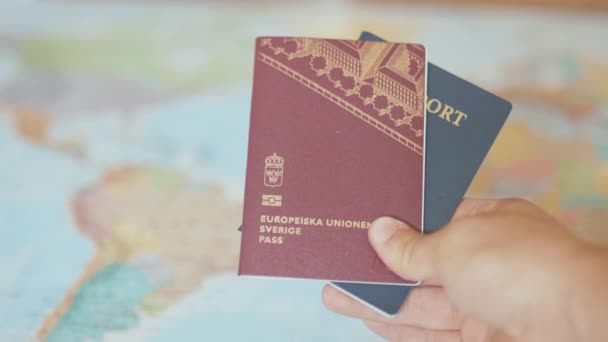 Hand in Hand mit einem schwedischen und einem amerikanischen Pass vor einer bunten Weltkarte — Stockvideo