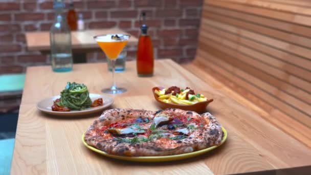 Vegan pizza, a cocktail, zucchini noodles, and fries on a wooden table — Stock Video