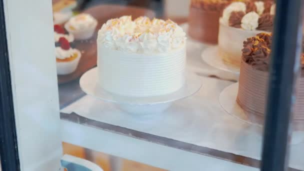 Vanilla buttercream and chocolate cakes through the window of a bakery — Video Stock