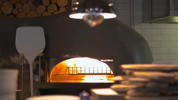 Vuur pizza oven naast een pizza schop en achter een wazig verlichte tafel — Stockvideo
