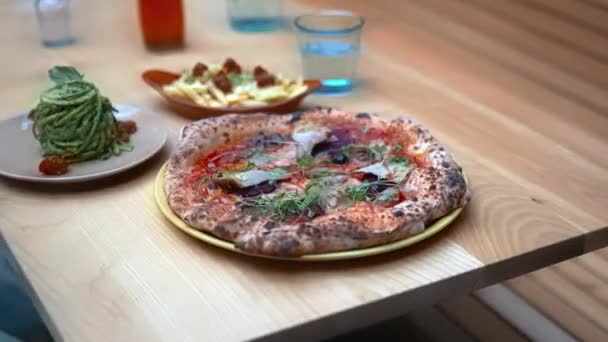 Vegan pizza, and other vegan dishes on a wooden table surrounded by seats — Stock Video