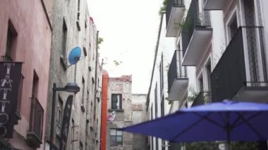 Backwards Moving View of an Alley with Blue Umbrellas and a Tattoo Studio