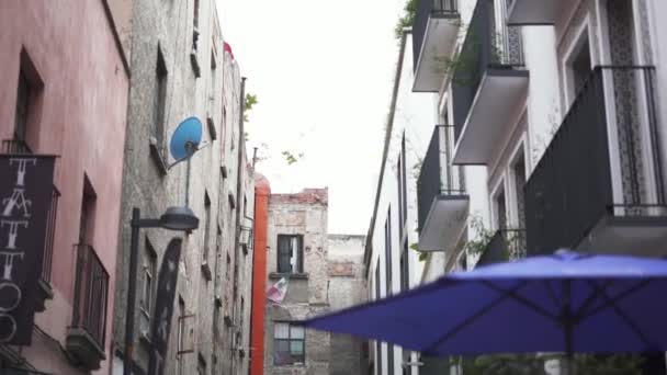 Rückwärts bewegender Blick auf eine Gasse mit blauen Regenschirmen und einem Tätowierstudio — Stockvideo