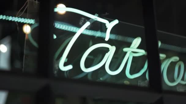 Cartel de luz de tatuaje azul en una ventana de una barbería y un estudio de tatuajes — Vídeo de stock