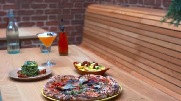 Vegan pizza, a cocktail, zucchini noodles, and fries on a wooden table — Stock Video