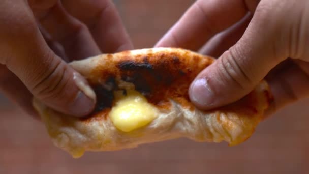 Two hands breaking a cheesy dough ball in two showing its cheese filling — Wideo stockowe