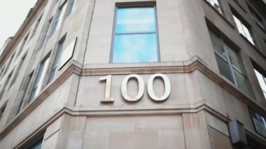 Gri bir binanın köşesindeki pencerenin altında 100 numaralı adres.