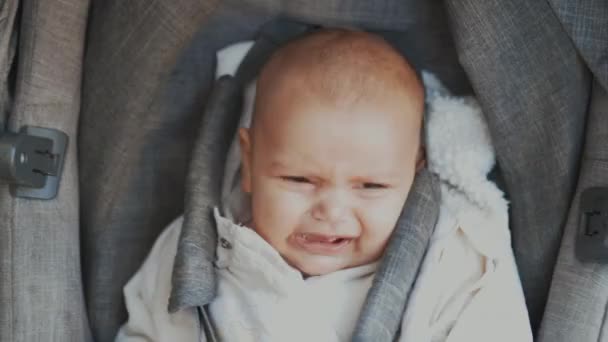 Κλαίγοντας μωρό σε ένα γκρι καρότσι κοιτάζοντας θλιμμένα την κάμερα — Αρχείο Βίντεο