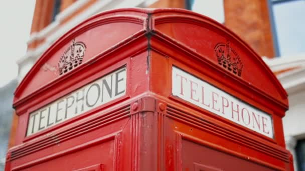 Egy londoni telefonfülke tetején, háttérként homályos téglaépülettel. — Stock videók