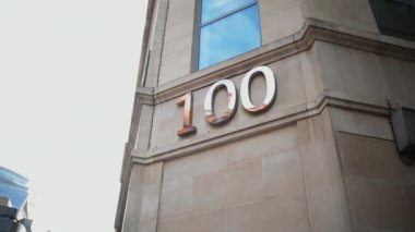Gri bir binanın köşesindeki pencerenin altında 100 numaralı adres.