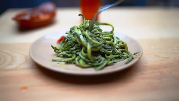 Mano che fa girare una forchetta in un piatto di tagliatelle di zucchine su un tavolo di legno — Video Stock