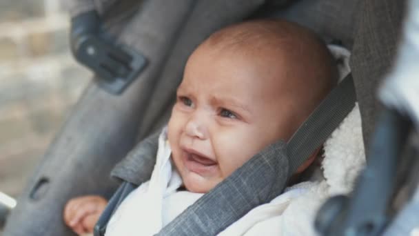 Bebê chorando em um carrinho cinza olhando dolorosamente para a câmera — Vídeo de Stock