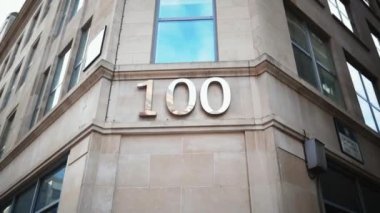 Gri bir binanın köşesindeki pencerenin altında 100 numaralı adres.