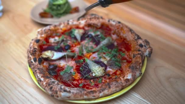 Dressing a thick vegan pizza with oily salad dressing on a wooden table — Stock Video