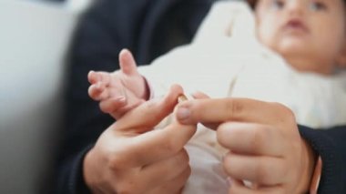 Annesinin başparmağını tutan bir bebeğin küçük elinin yakın görüntüsü.