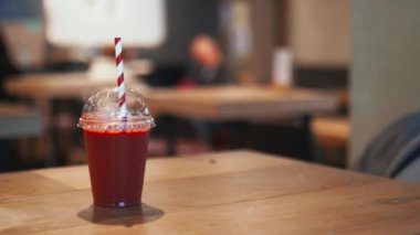 Ahşap bir restoran masasında kırmızı ve beyaz çizgili kamış ile kırmızı smoothie.