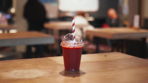 Smoothie vermelho com uma palha listrada vermelha e branca em uma mesa de restaurante de madeira — Vídeo de Stock