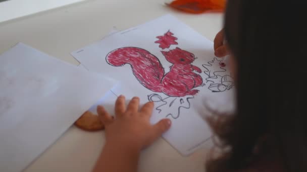 Little girl coloring a squirrel image on a paper sheet with a red marker — Wideo stockowe