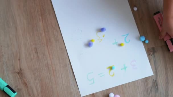 Bolas de algodón coloridas y sumas en una hoja de papel blanco junto con una pequeña mano — Vídeo de stock