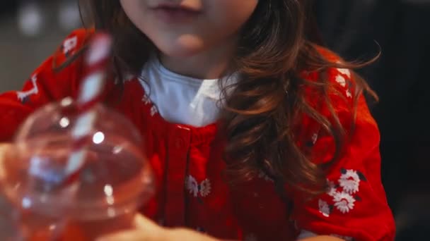 Happy little girl adorably sipping her red smoothie with a striped straw — Wideo stockowe