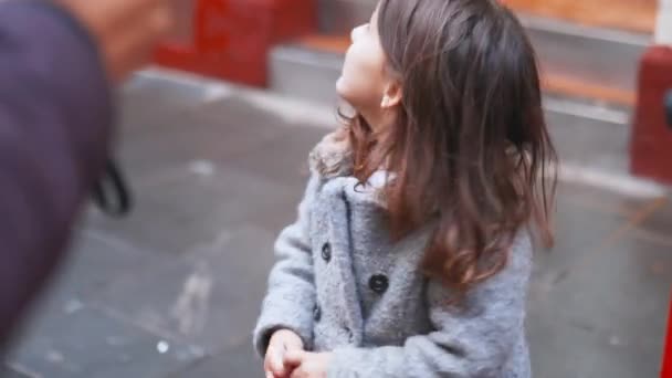 Little girl on the sidewalk looks behind her when two people pass by next to her — Stock Video