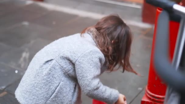 Menina morena em um casaco cinza na calçada segurando um saco de plástico vermelho — Vídeo de Stock