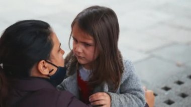 Siyah maskeli bir kadın, küçük üzgün kızını teselli etmek için kucaklıyor.