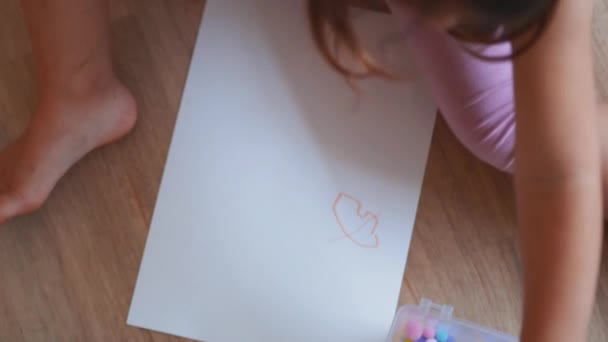 Little girl sitting on the floor and pacing cotton balls on a paper sheet Video Clip