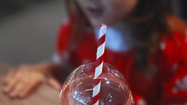 Happy little girl adorably sipping her red smoothie with a striped straw — Wideo stockowe