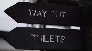 Wooden pole with indications pointing out where are the toilets and the exit