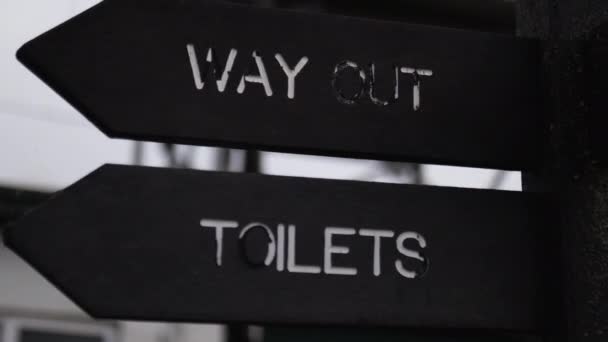 Wooden pole with indications pointing out where are the toilets and the exit — Vídeo de Stock