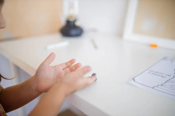 Paint stains on the hands of a little girl resting above a white desk — Stock fotografie