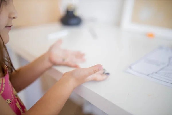 Paint stains on the hands of a little girl resting above a white desk — Stock fotografie