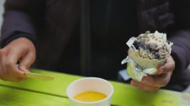 Woman sitting at a table and adding yellow sauce on a meat and cheese burrito