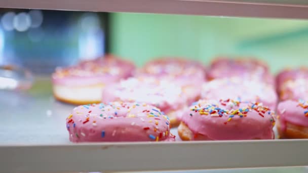 Close up view of pink glazed doughnuts covered with colorful sprinkles — Stockvideo