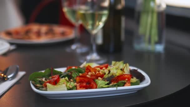Gourmet salad alongside two wine glasses and a bottle of wine on a black table — Wideo stockowe