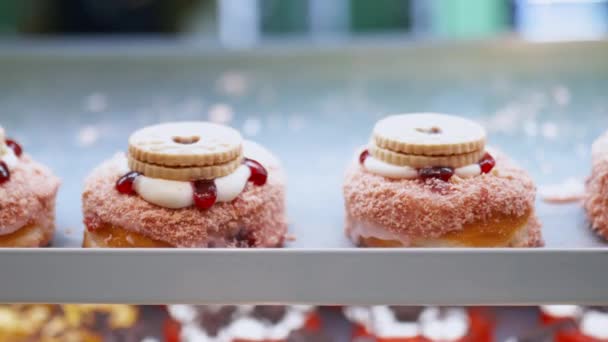 Közelkép a rózsaszín öntetű fánkokról és sütikről egy pékségben — Stock videók