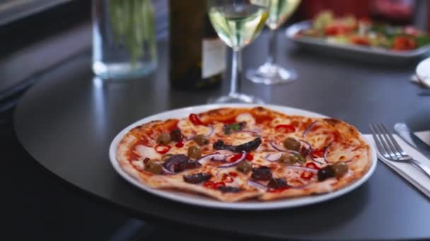 Gurmánská pizza vedle dvou sklenic na víno a láhev vína na černém stole — Stock video