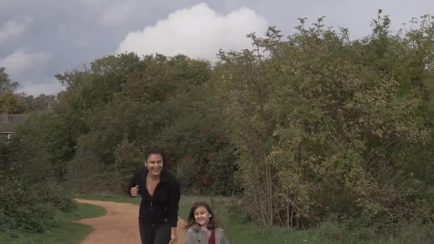 Feliz niña y su madre corriendo por un camino de tierra rodeado de árboles — Vídeos de Stock