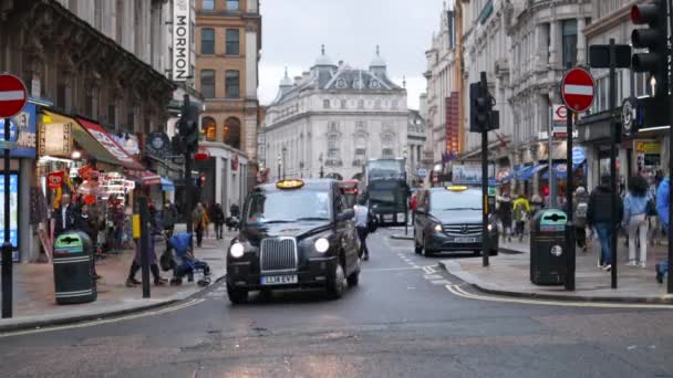 Front view of a crowded one-way street with a classic London taxi turning right — Αρχείο Βίντεο