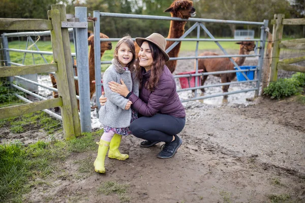 Felice madre e figlia sorridente con alpaca marroni dietro di loro — Foto Stock