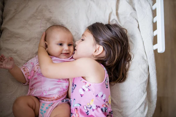 Klein meisje liggend op een bed en vreedzaam knuffelen haar gelukkig zusje — Stockfoto