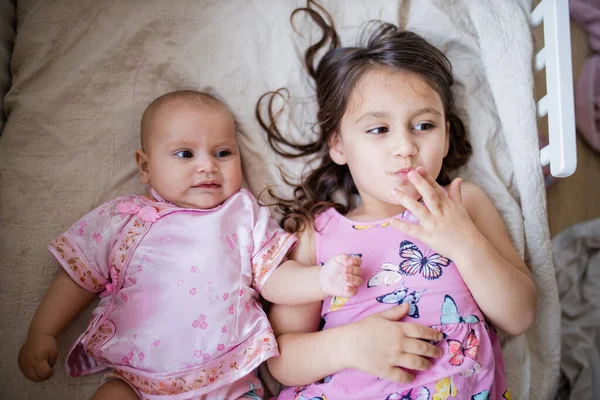 Menina feliz e irmã bebê em roupas rosa deitado em uma cama — Fotografia de Stock